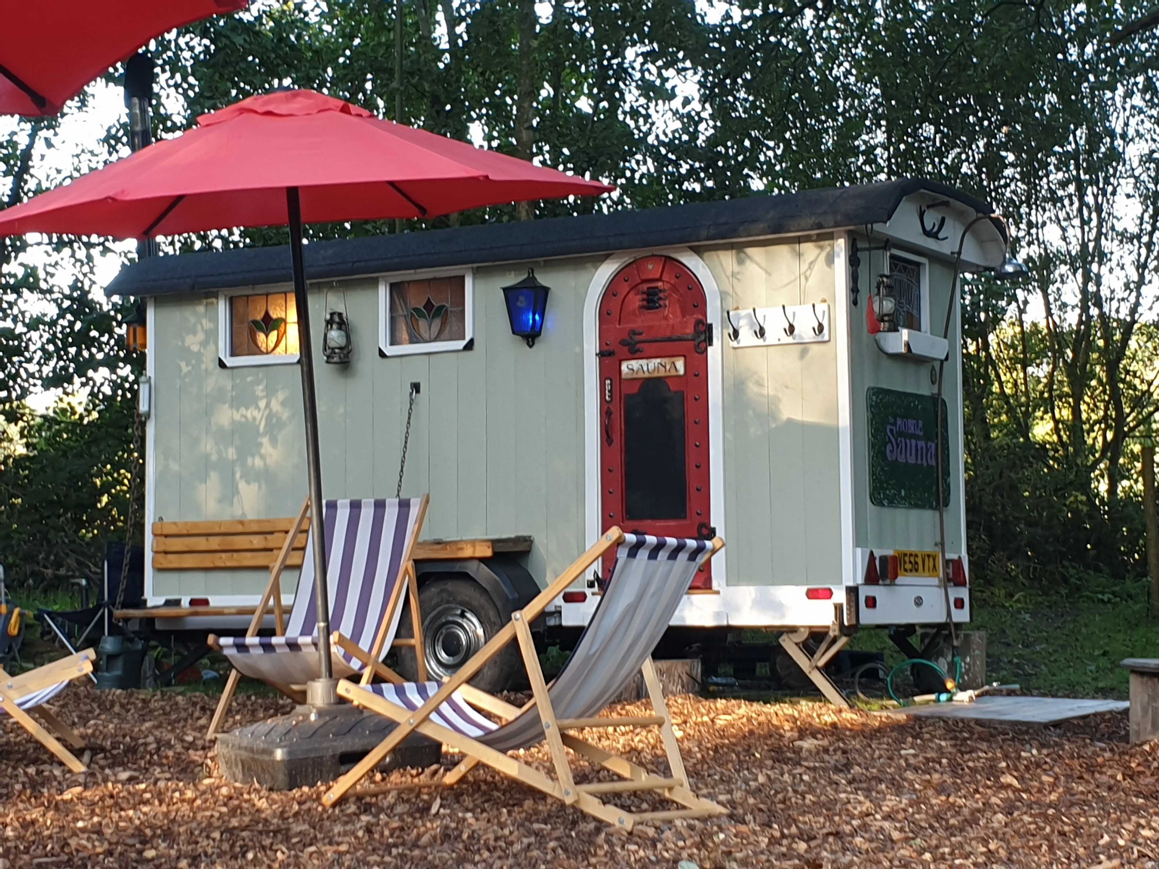 The full length of the shepherd’s hut sauna, with red umbrellas and deckchairs set out in front